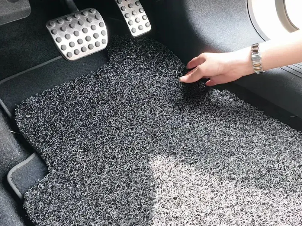 A universal coil mat in a driver's footwell: a gap along its left edge, the mat creeping up to the pedal, and a hand shifting its far corner